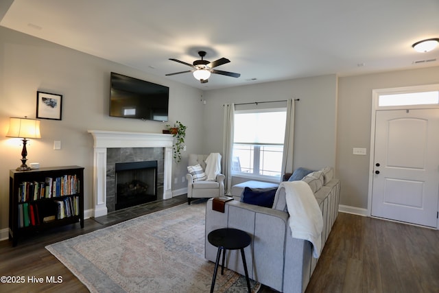 living room with baseboards, dark wood-type flooring, ceiling fan, and a tiled fireplace