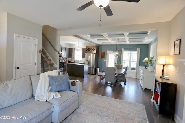 living room with beamed ceiling, dark wood-type flooring, a ceiling fan, coffered ceiling, and stairs