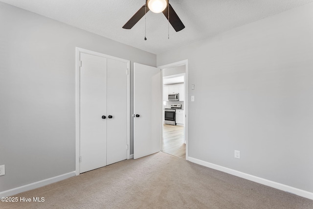 unfurnished bedroom with light carpet, a textured ceiling, a closet, baseboards, and ceiling fan