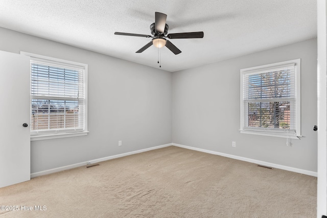 carpeted empty room featuring plenty of natural light, a ceiling fan, baseboards, and a textured ceiling