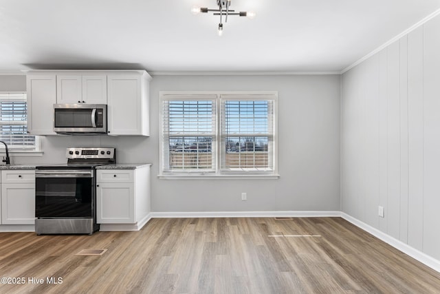 kitchen with light wood-style floors, appliances with stainless steel finishes, ornamental molding, and white cabinetry