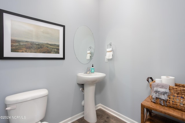 bathroom with toilet, wood finished floors, baseboards, and a sink