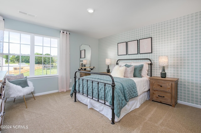 carpeted bedroom featuring wallpapered walls, visible vents, baseboards, and an accent wall