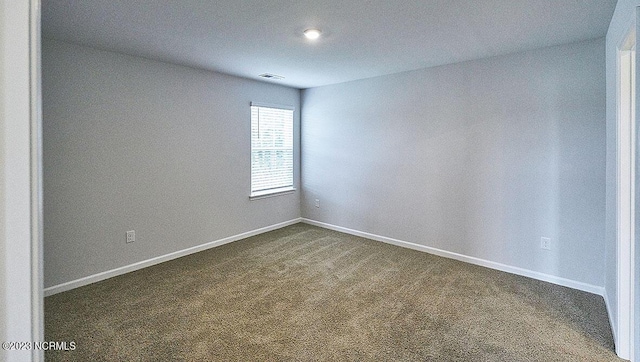 unfurnished room with dark colored carpet, visible vents, and baseboards