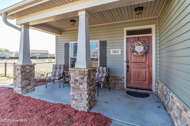 doorway to property with stone siding, a porch, and fence