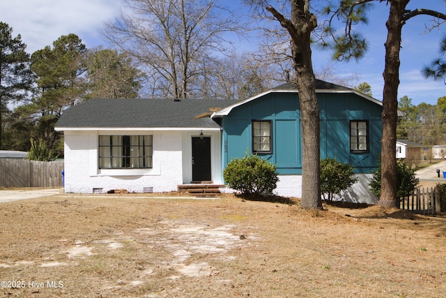 view of front of house with crawl space, brick siding, a shingled roof, and fence