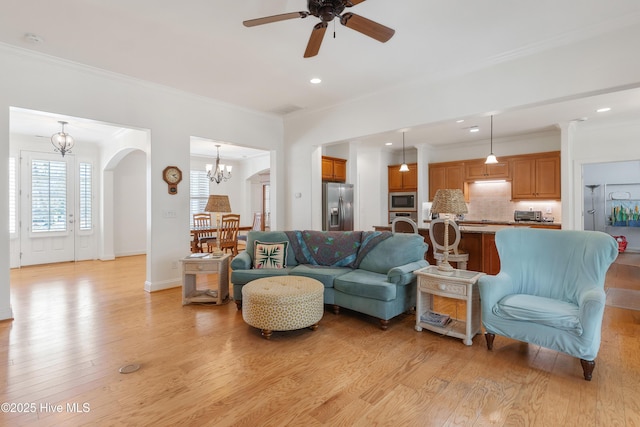 living area featuring arched walkways, ceiling fan with notable chandelier, light wood-type flooring, and ornamental molding