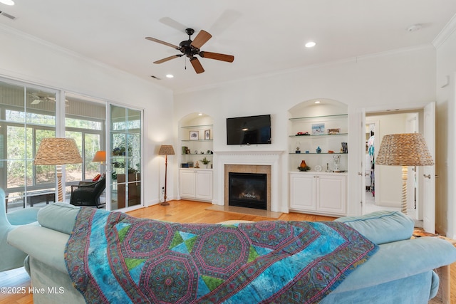 living room with ornamental molding, built in shelves, light wood-style floors, and ceiling fan