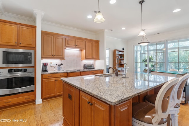 kitchen with light stone counters, an island with sink, built in microwave, a sink, and oven