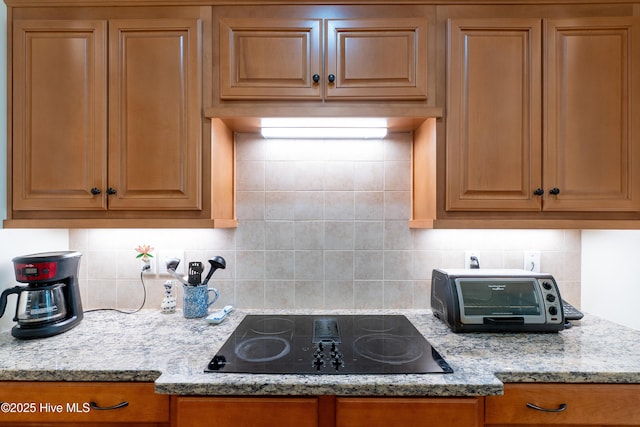 kitchen with a toaster, black electric stovetop, light stone counters, and backsplash