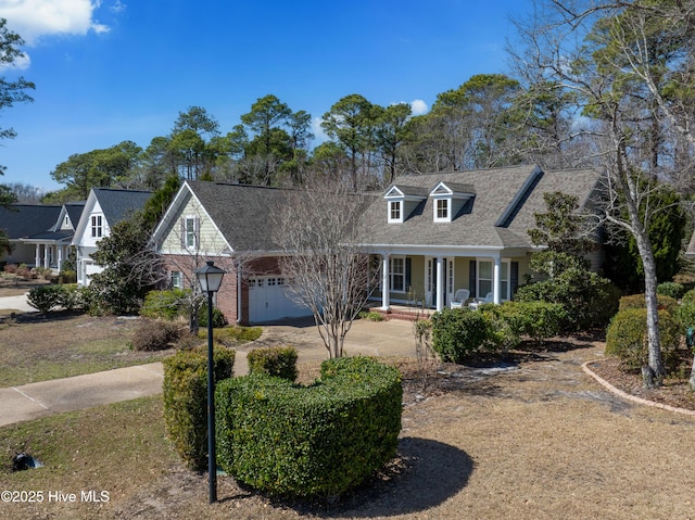 cape cod-style house featuring driveway, a porch, an attached garage, a shingled roof, and brick siding