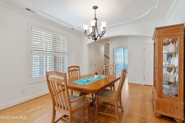 dining area with visible vents, crown molding, light wood-style flooring, an inviting chandelier, and arched walkways