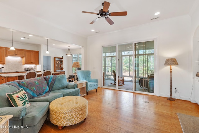 living room featuring visible vents, crown molding, light wood-type flooring, and a ceiling fan