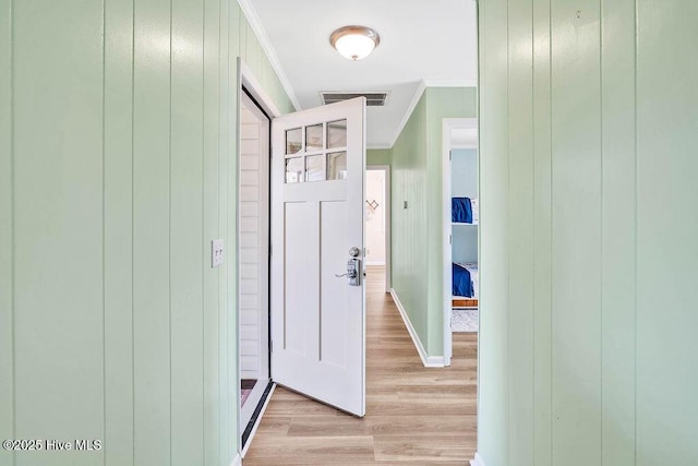 hallway with visible vents, light wood-type flooring, baseboards, and ornamental molding