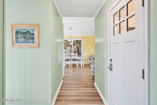 hallway with light wood-style flooring, baseboards, a chandelier, and ornamental molding