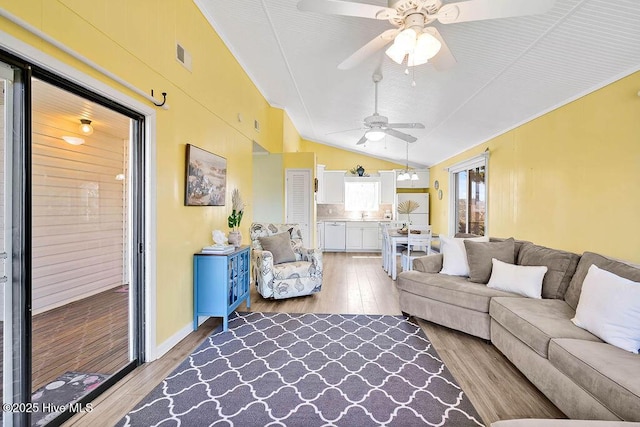 living room with light wood-type flooring, visible vents, a ceiling fan, and vaulted ceiling