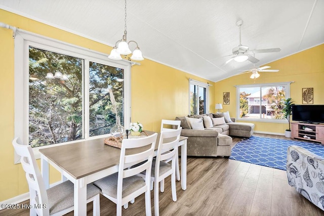 dining area featuring ceiling fan with notable chandelier, wood finished floors, and vaulted ceiling