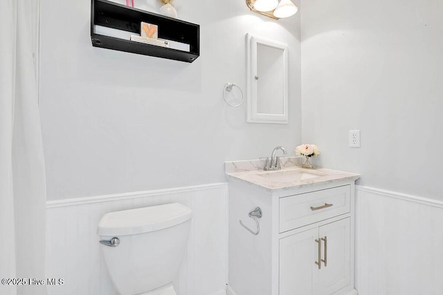 half bath featuring a wainscoted wall, toilet, and vanity