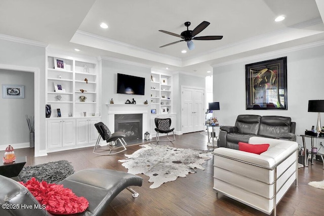 living area featuring a fireplace with flush hearth, dark wood-type flooring, a tray ceiling, and a ceiling fan