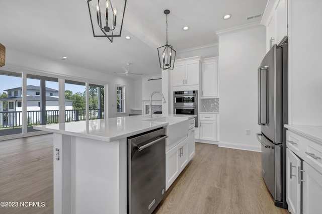 kitchen with a sink, stainless steel appliances, light wood-style floors, ceiling fan with notable chandelier, and tasteful backsplash