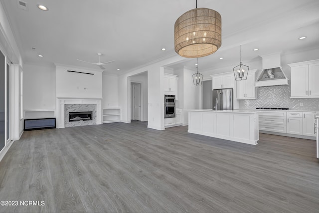 unfurnished living room featuring recessed lighting, wood finished floors, a high end fireplace, and ceiling fan with notable chandelier