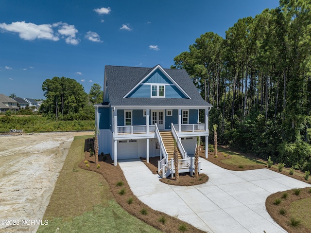 coastal home with roof with shingles, an attached garage, covered porch, stairs, and concrete driveway