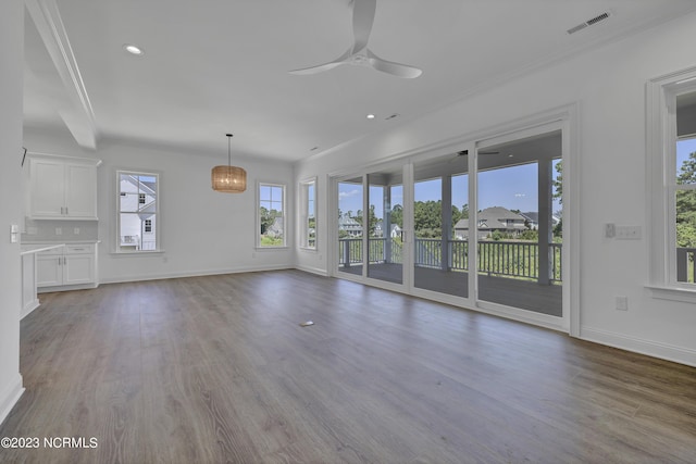 unfurnished living room with a ceiling fan, wood finished floors, visible vents, baseboards, and crown molding