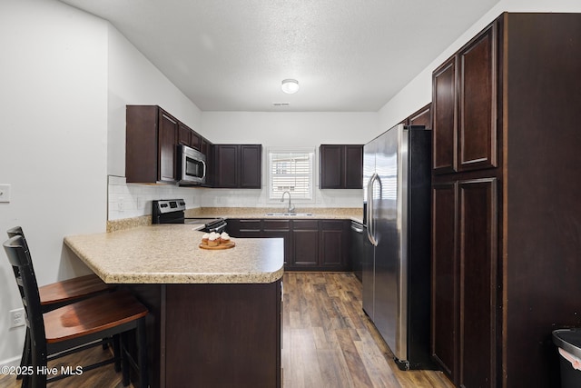 kitchen with a peninsula, stainless steel appliances, light countertops, dark wood-type flooring, and dark brown cabinets