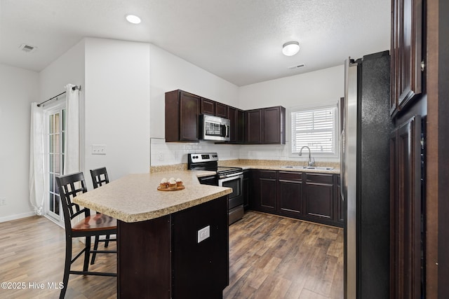 kitchen featuring a peninsula, light countertops, dark brown cabinets, appliances with stainless steel finishes, and a kitchen breakfast bar