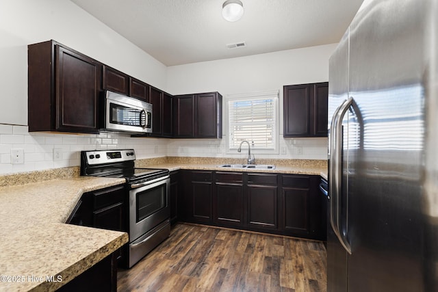 kitchen with visible vents, a sink, decorative backsplash, stainless steel appliances, and dark wood-style flooring