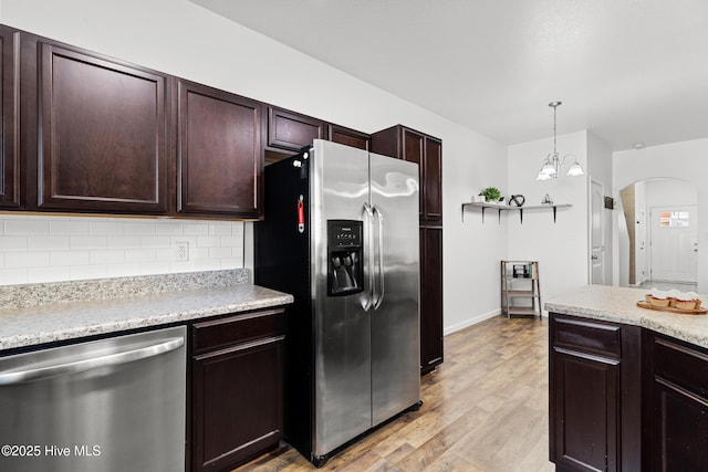 kitchen featuring stainless steel appliances, arched walkways, light wood-style floors, light countertops, and decorative backsplash