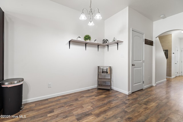 spare room featuring baseboards, arched walkways, wood finished floors, and a chandelier