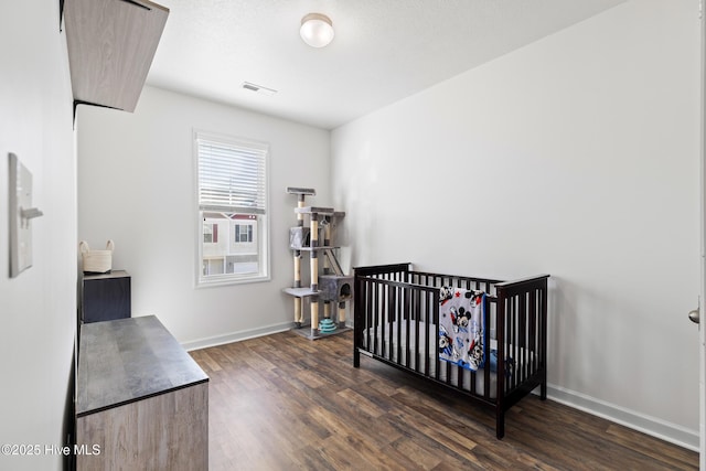 bedroom featuring dark wood-style floors, visible vents, a crib, and baseboards