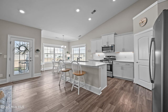 kitchen with dark wood-style floors, a center island with sink, appliances with stainless steel finishes, and light countertops