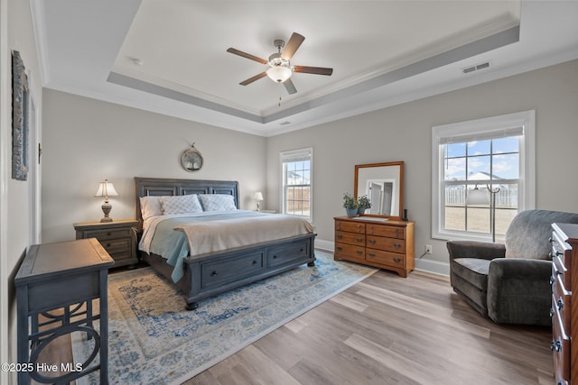 bedroom with visible vents, light wood-type flooring, a raised ceiling, and baseboards