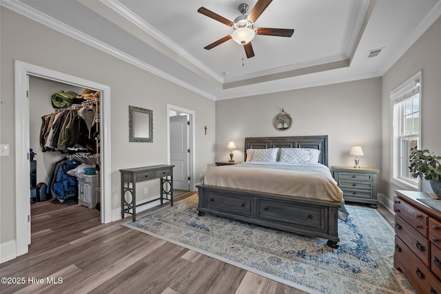 bedroom featuring a walk in closet, visible vents, ornamental molding, a tray ceiling, and wood finished floors