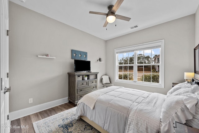 bedroom featuring ceiling fan, visible vents, baseboards, and wood finished floors