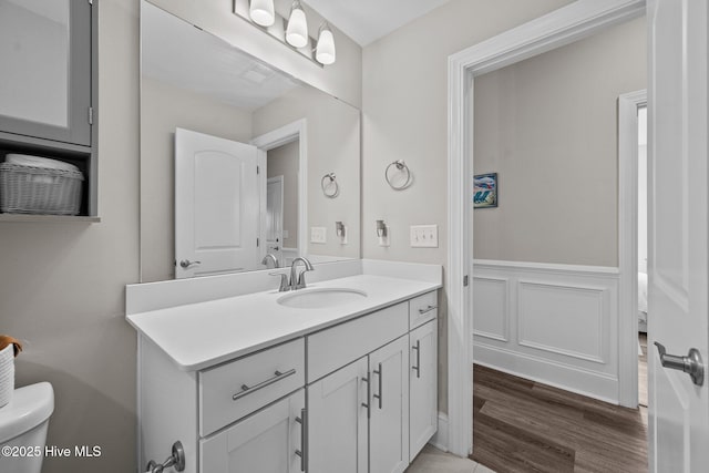 bathroom featuring a wainscoted wall, toilet, wood finished floors, a decorative wall, and vanity