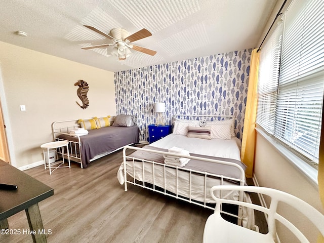 bedroom featuring wood finished floors, baseboards, ceiling fan, a textured ceiling, and an accent wall