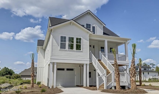 coastal inspired home featuring a porch, concrete driveway, an attached garage, a shingled roof, and stairs