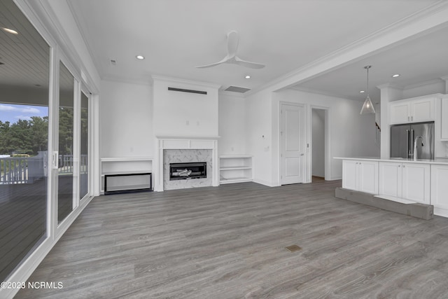 unfurnished living room featuring a high end fireplace, crown molding, light wood finished floors, and ceiling fan