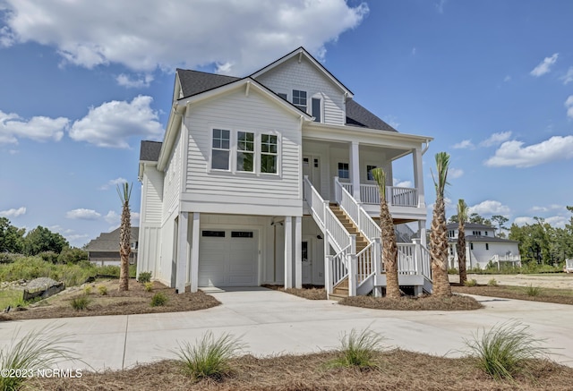 coastal home with a porch, stairway, concrete driveway, an attached garage, and a shingled roof