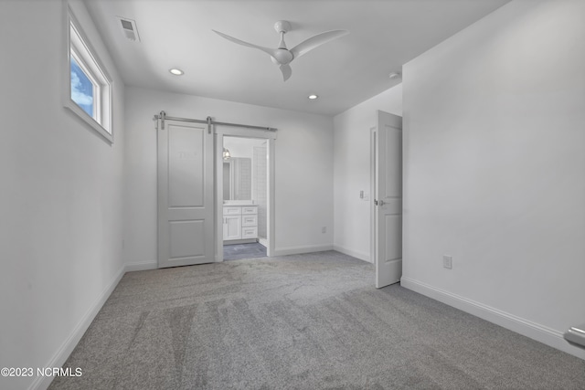 unfurnished bedroom with visible vents, ensuite bath, a barn door, carpet, and baseboards