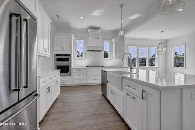 kitchen with white cabinets, appliances with stainless steel finishes, custom range hood, and a kitchen island with sink