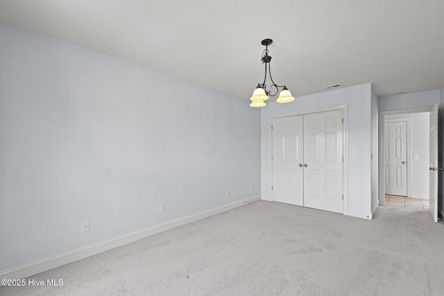 unfurnished bedroom featuring visible vents, a closet, an inviting chandelier, baseboards, and light colored carpet