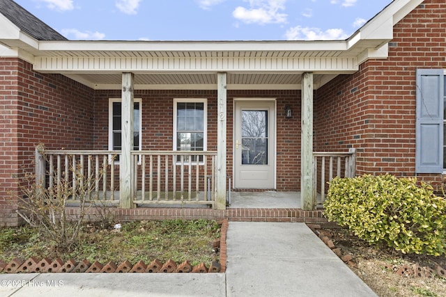 view of exterior entry with brick siding and covered porch