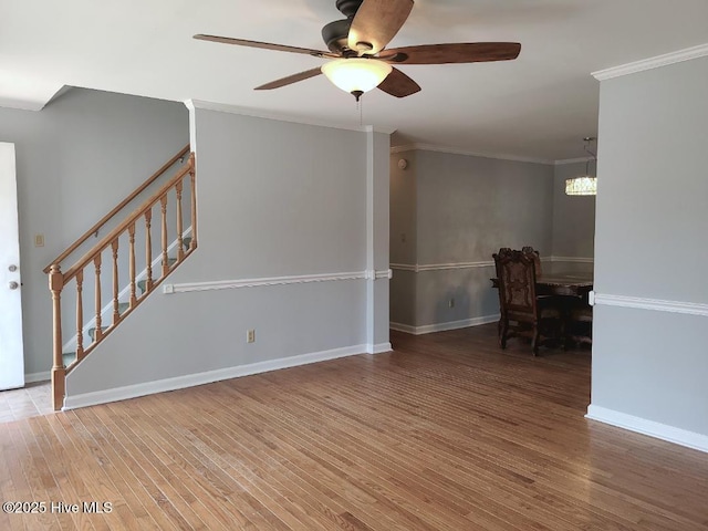 unfurnished room featuring stairway, wood finished floors, baseboards, ornamental molding, and ceiling fan with notable chandelier