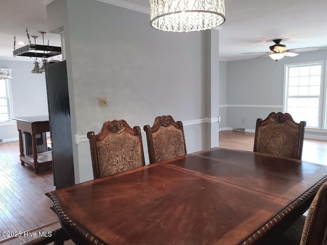 dining area featuring ceiling fan with notable chandelier, crown molding, wood finished floors, and baseboards