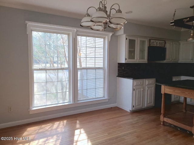 kitchen with baseboards, light wood finished floors, white cabinetry, a notable chandelier, and backsplash