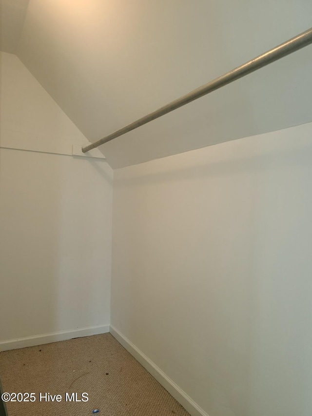 walk in closet with light colored carpet and vaulted ceiling